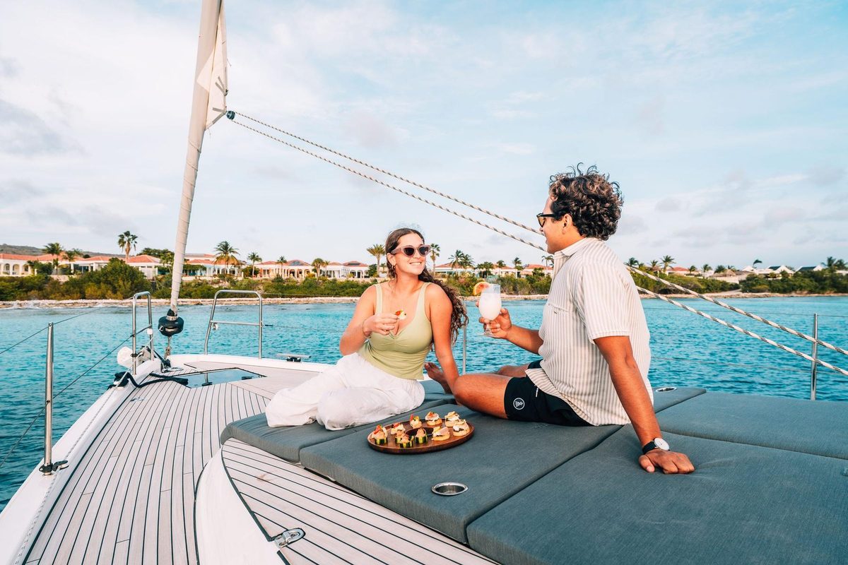 Couple on the bow of the Compass Bonaire at golden hour with canapés and a cocktail